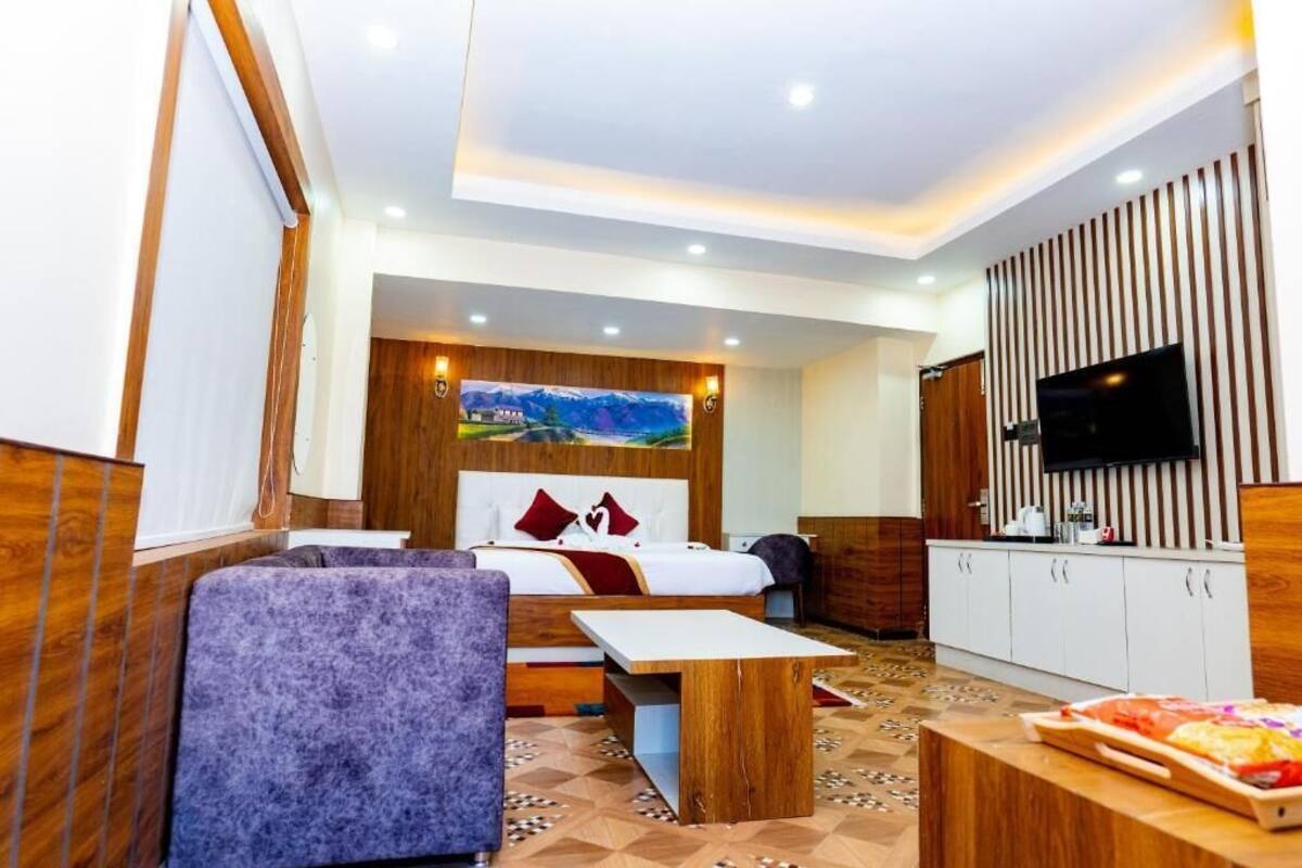 A hotel room with a bed, a seating area, a TV, and a kitchen area.