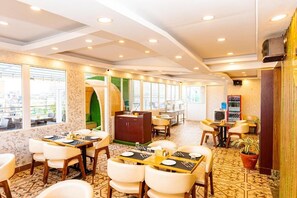 Un restaurant avec des tables dressées pour le service, un coin bar et une vue dégagée grâce à de grandes fenêtres.