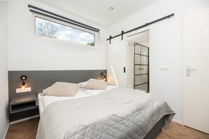 A bedroom with a bed, bedside tables, a window, a sliding door, and a wall-mounted light fixture.
