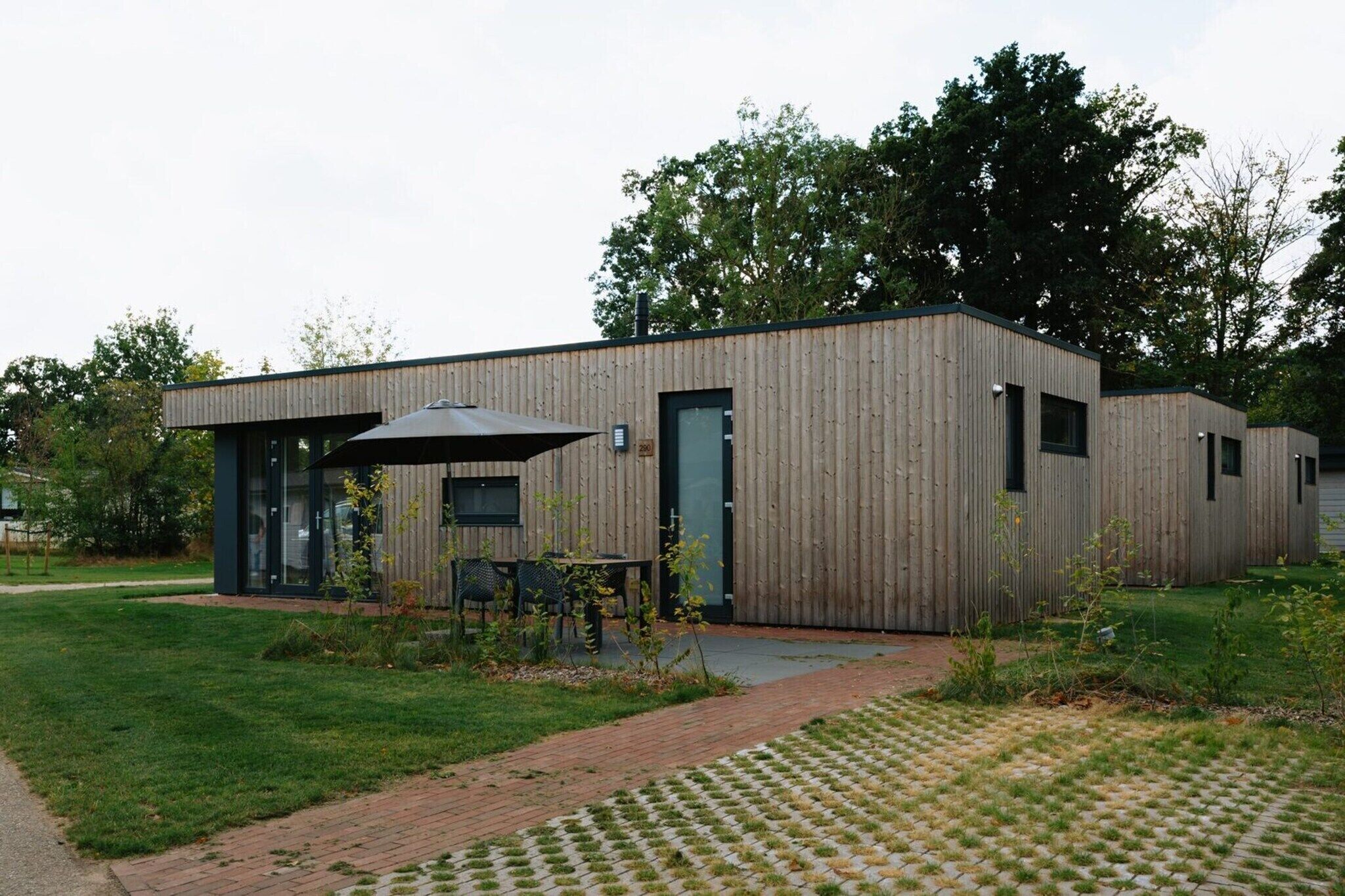 Ein modernes Gebäude mit Holzfassade, einer überdachten Außenbereich-Sitzgelegenheit und einem gepflasterten Weg.