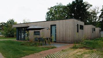Ein modernes Gebäude mit Holzfassade, einer überdachten Außenbereich-Sitzgelegenheit und einem gepflasterten Weg.