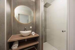 Ein modernes Badezimmer mit rundem Spiegel, einem Aufsatzwaschbecken und einer Duschkabine.