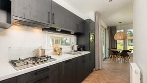 Une cuisine moderne avec des meubles de couleur sombre, une cuisinière à gaz et une fenêtre donnant sur un coin repas.