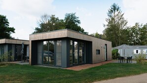 Un bâtiment moderne doté de grandes fenêtres en verre, d’une façade en bois et d’une pelouse dallée.