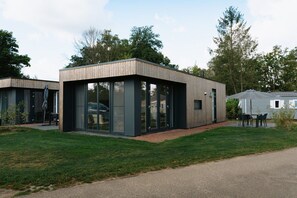 Ein modernes Gebäude mit großen Glasfenstern, einer Holzfassade und einer gepflasterten Rasenfläche.