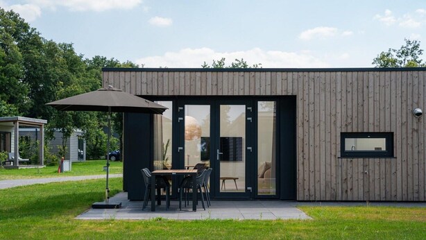 Un bâtiment moderne avec une façade en bois, une entrée dotée d’une porte en verre et un patio comprenant une table et des chaises.