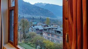 Vista a través de una ventana con marcos de madera, que da a una ciudad con edificios y montañas al fondo.