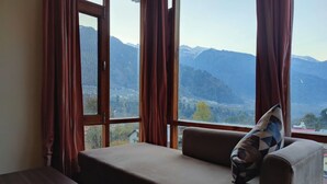 Una habitación con sofá y mesa, una ventana con cortinas y vistas a montañas.