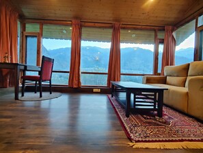 Una habitación con techo de madera, ventanas amplias con cortinas, un sofá, una mesa y una silla.
