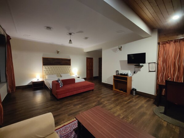 Habitación de hotel con una cama, un sofá rojo, un televisor, suelo de madera y un ventilador de techo.