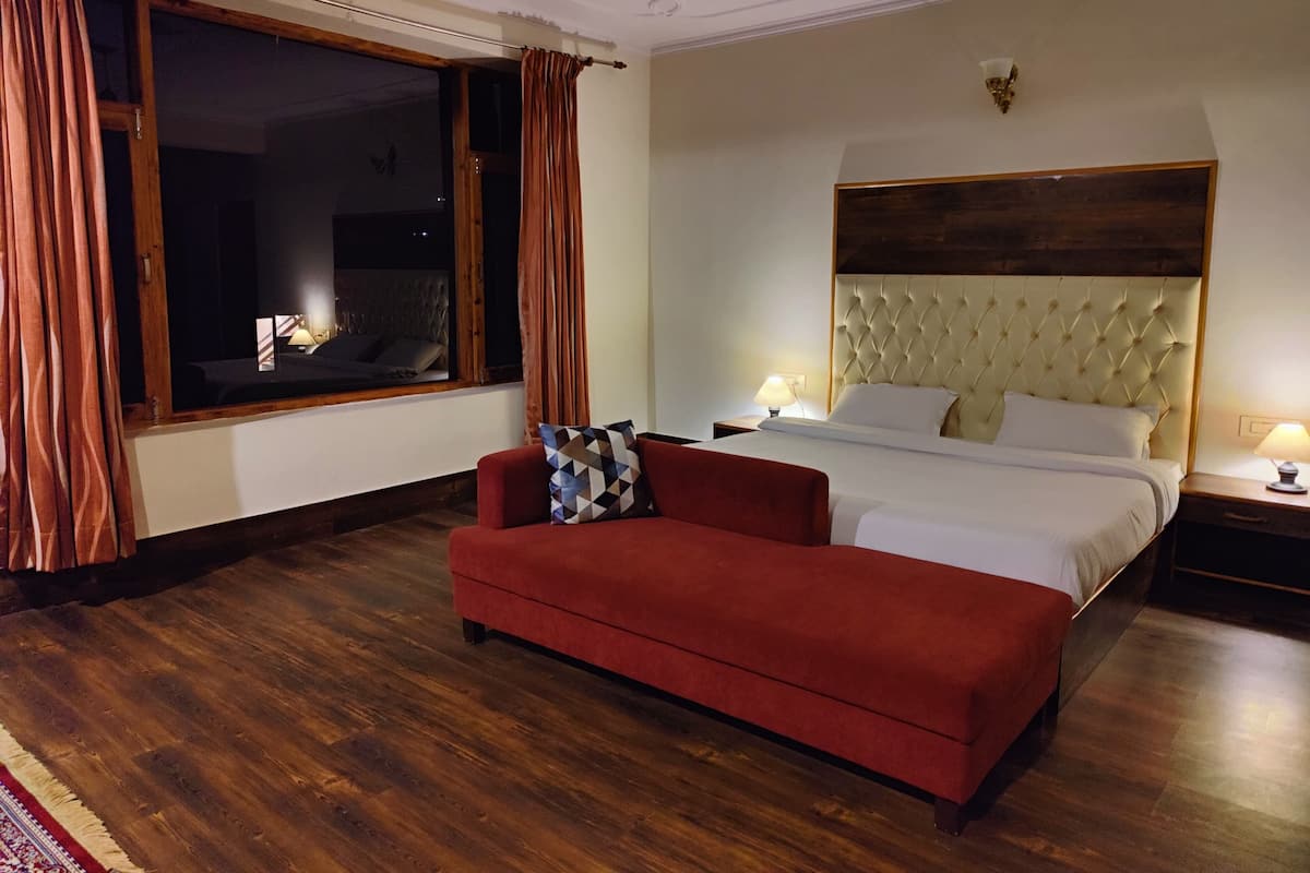 Un dormitorio con un ventanal grande, una cama con cabecera capitonada, un sofá rojo y una mesita de noche con lámpara.