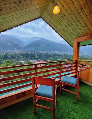 Un balcón de madera con dos sillas y una lámpara colgante, con vistas a un paisaje montañoso.