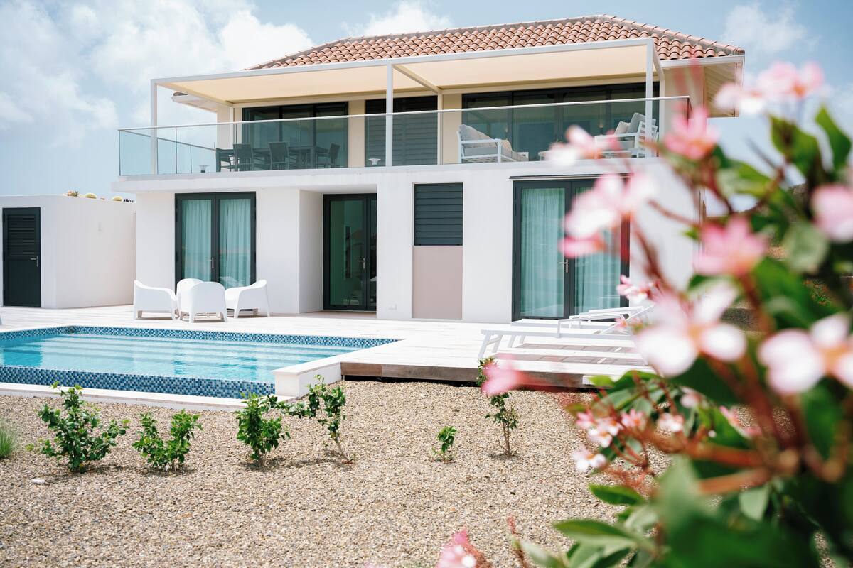 Una casa moderna de dos pisos con piscina, mobiliario exterior y un balcón.