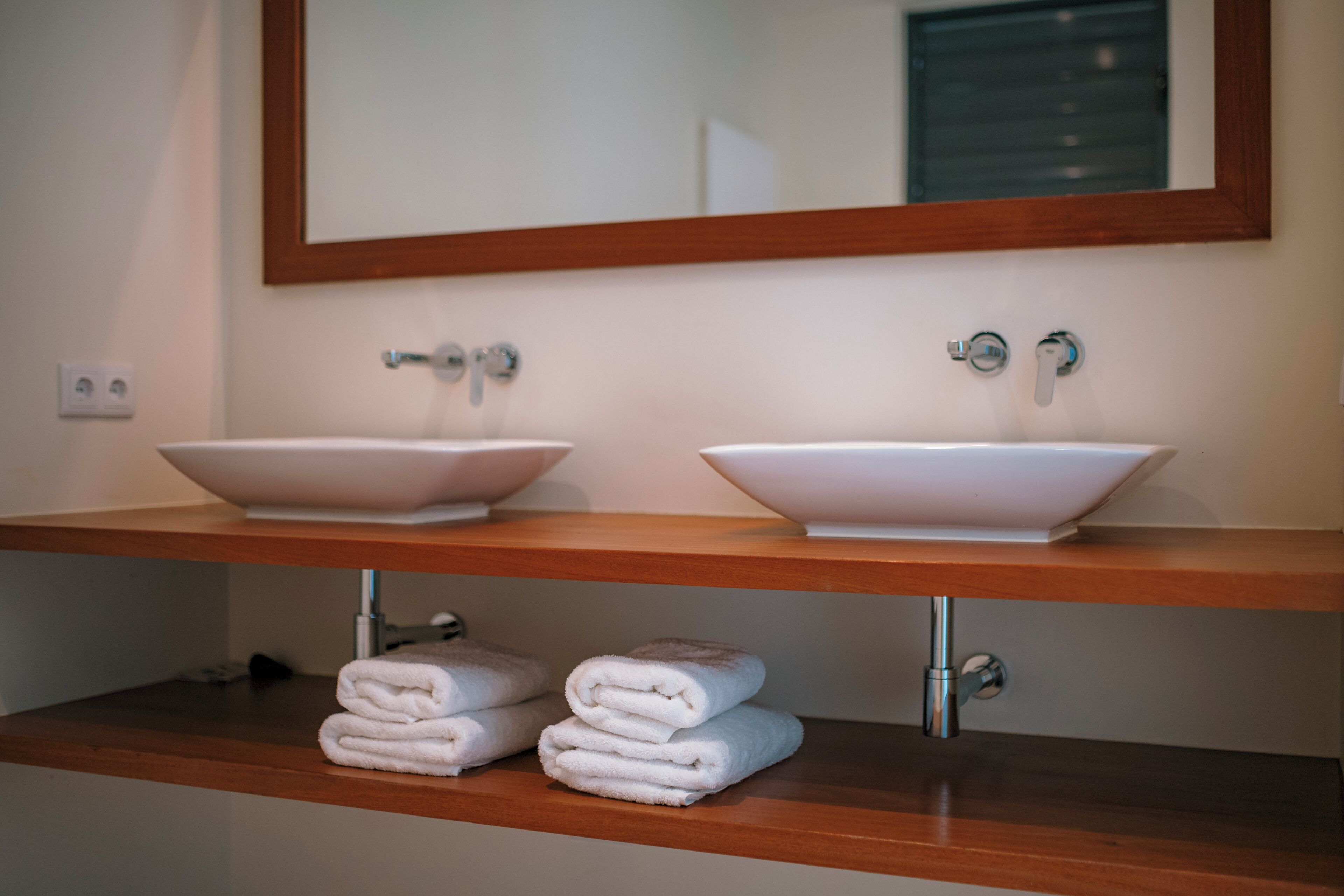 Un baño con dos lavamanos blancos, un mueble de tocador de madera y un espejo sobre los lavamanos.