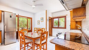 Una cocina con refrigerador de acero inoxidable, mesa y sillas de madera, y ventanas que dan a zonas verdes.