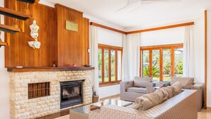 Una sala de estar con chimenea de piedra, paneles de madera, un conjunto de sofás y ventanas grandes.