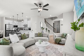 Ein modernes Wohnzimmer mit einer Couch, einem Couchtisch und einem Essbereich, im Hintergrund eine Küche.
