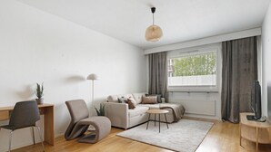 Una sala de estar moderna con piso de madera, un sofá, una silla, una mesita, un televisor y una ventana con cortinas.