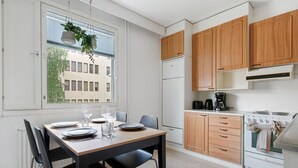 Una cocina moderna con armarios de madera, una mesa de comedor preparada para cuatro personas y un ventanal con vistas a edificios.