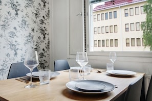 Ein Esstisch ist gedeckt mit Tellern, Gläsern und Besteck, ein Stuhl und ein Fenster mit Blick auf ein Gebäude.