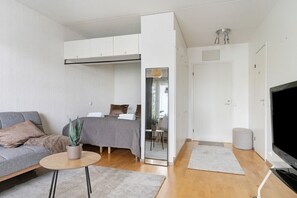 Ein kompakter Wohnraum mit Sofa, Bett, kleinem Tisch, Fernseher und einer Schiebetür zu einem weiteren Zimmer.