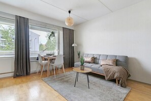 Ein modernes Wohnzimmer mit grauem Sofa, rundem Couchtisch, Esstisch mit Stühlen und einer hängenden Pflanze.