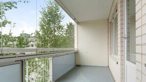 Parveke, josta avautuu näkymä puille ja rakennuksille, valkoiset laatat lattiassa ja valkoinen seinä.
