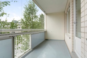 Ein Balkon mit Blick auf Bäume und Gebäude, ein weiß gefliester Boden und eine weiße Wand.