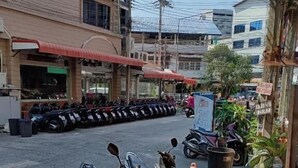 A street view with parked motorcycles, a building with a red awning, and a signboard. - Del Mar Hotel (Pattaya)
