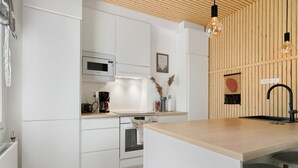 Una cocina moderna con armarios blancos, encimera de madera, horno integrado, microondas, cafetera y grifo negro.