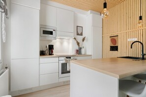 Eine moderne Küche mit weißen Schränken, einer Holz Arbeitsplatte, einem Einbauofen, einer Mikrowelle, einer Kaffeemaschine und einem schwarzen Wasserhahn.