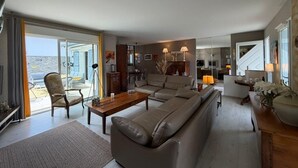 A spacious living room with a sofa, coffee table, and armchair, a dining area with a table and chairs, and a kitchen in the background. - La Villa Ametza - Swimming pool (MOUGUERRE)