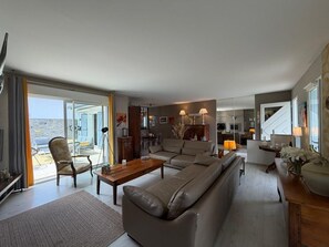 A spacious living room with a sofa, coffee table, and armchair, a dining area with a table and chairs, and a kitchen in the background. - La Villa Ametza - Swimming pool (MOUGUERRE)