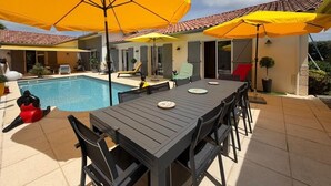 A poolside area with a table and chairs, yellow umbrellas, and a swimming pool. - La Villa Ametza - Swimming pool (MOUGUERRE)