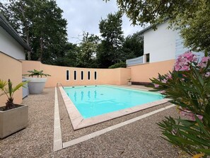 A rectangular swimming pool with a pebble-lined deck, surrounded by a low wall and potted plants. - L'Escale de Brindos - Collective pool (ANGLET)