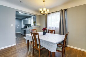 Een eetgedeelte met een tafel, stoelen, een kroonluchter en uitzicht op de keuken.