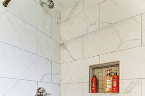 Een badkamer met marmeren tegels, een douchekop en een plank met toiletartikelen.