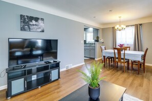 Un salon moderne doté d’un téléviseur à écran plat, d’un coin repas avec une table et des chaises, et d’une cuisine en arrière-plan.