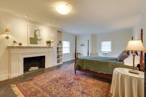 Un dormitorio con cama, chimenea, una alfombra grande y una mesita de noche.