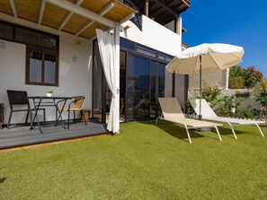 Eine moderne Außenpatio mit Tisch und Stühlen, einer Liege und einem überdachten Bereich mit einem weißen Sonnenschirm.