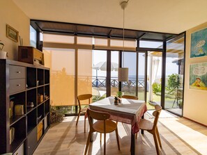 A dining area with a table and chairs, a bookshelf, and a view of the sea through large windows. - Komfortable Ferienwohnung in El Turman mit Garten, Terrasse by Interhome (Agaete)