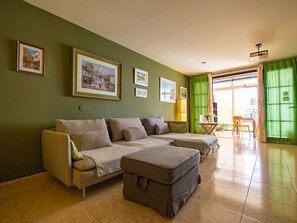 A living room with a sofa, ottoman, and a dining area with a table and chairs. - Komfortable Ferienwohnung in El Turman mit Garten, Terrasse by Interhome (Agaete)