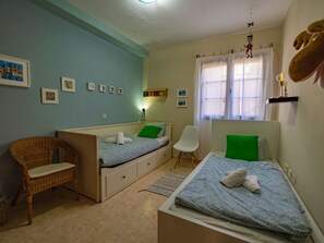 Ein Schlafzimmer mit zwei Betten, einem Sessel, einer Kommode und einem Fenster mit Vorhängen.