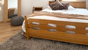 Een slaapkamer met een houten bed, een spiegel, een nachtkastje, een lamp en een raam met gordijnen.