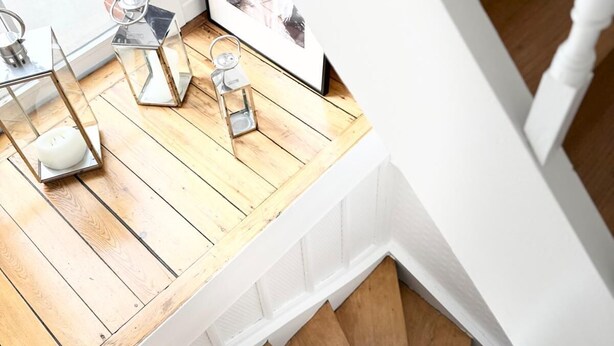 Een houten trap met witte leuningen, een raam met uitzicht op een bakstenen muur en een klein tafeltje met een kaars en een fotolijst.
