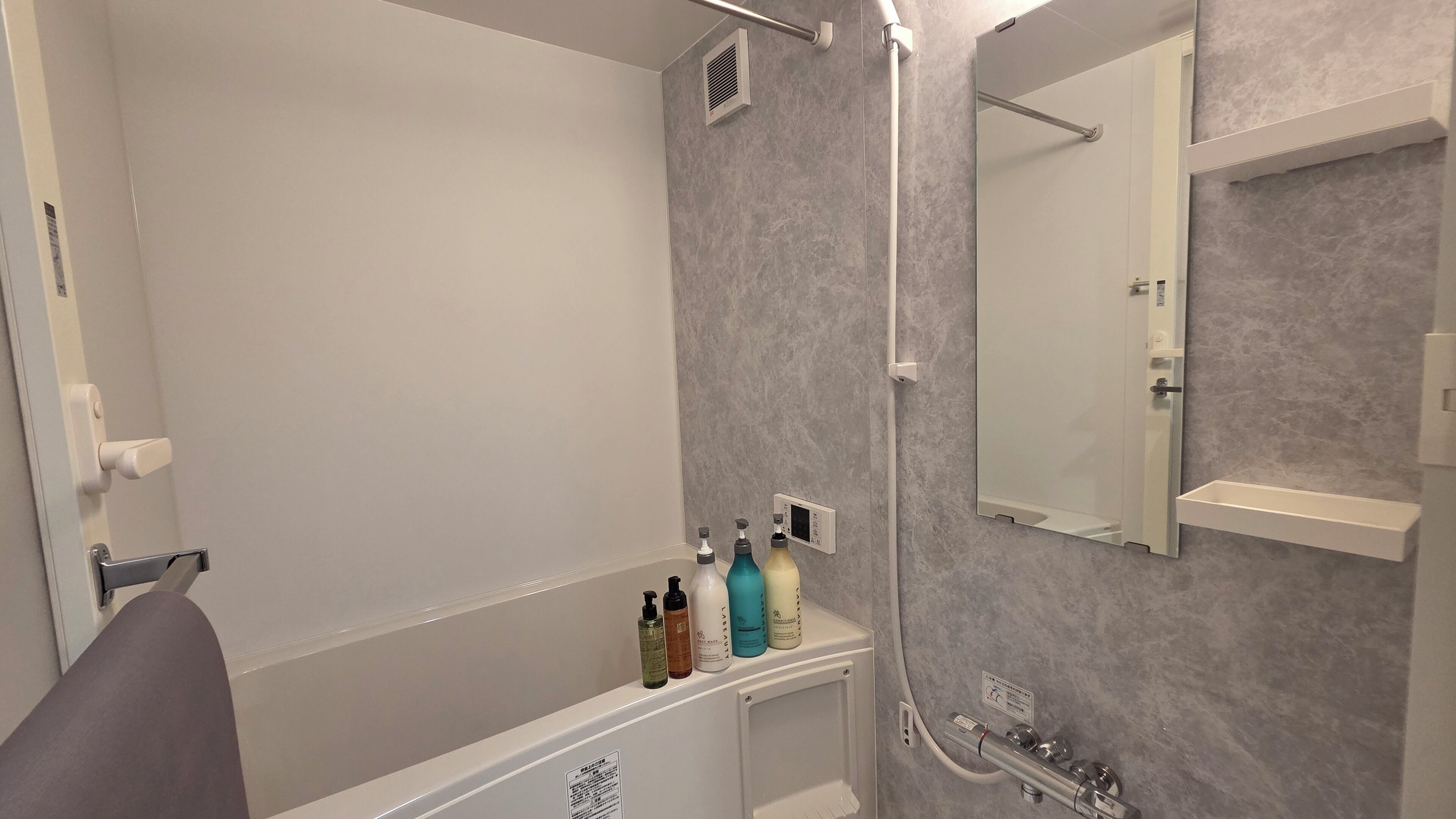 Une salle de bain moderne avec une baignoire, une douche, des toilettes et un lavabo. On trouve des articles de toilette sur le lavabo et un miroir au-dessus.