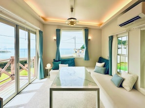 Una habitación moderna con una mesa de vidrio, cojines color turquesa y vistas al mar.