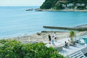 Una zona costera con una terraza de madera con vista al mar, una playa de arena y un litoral rocoso.