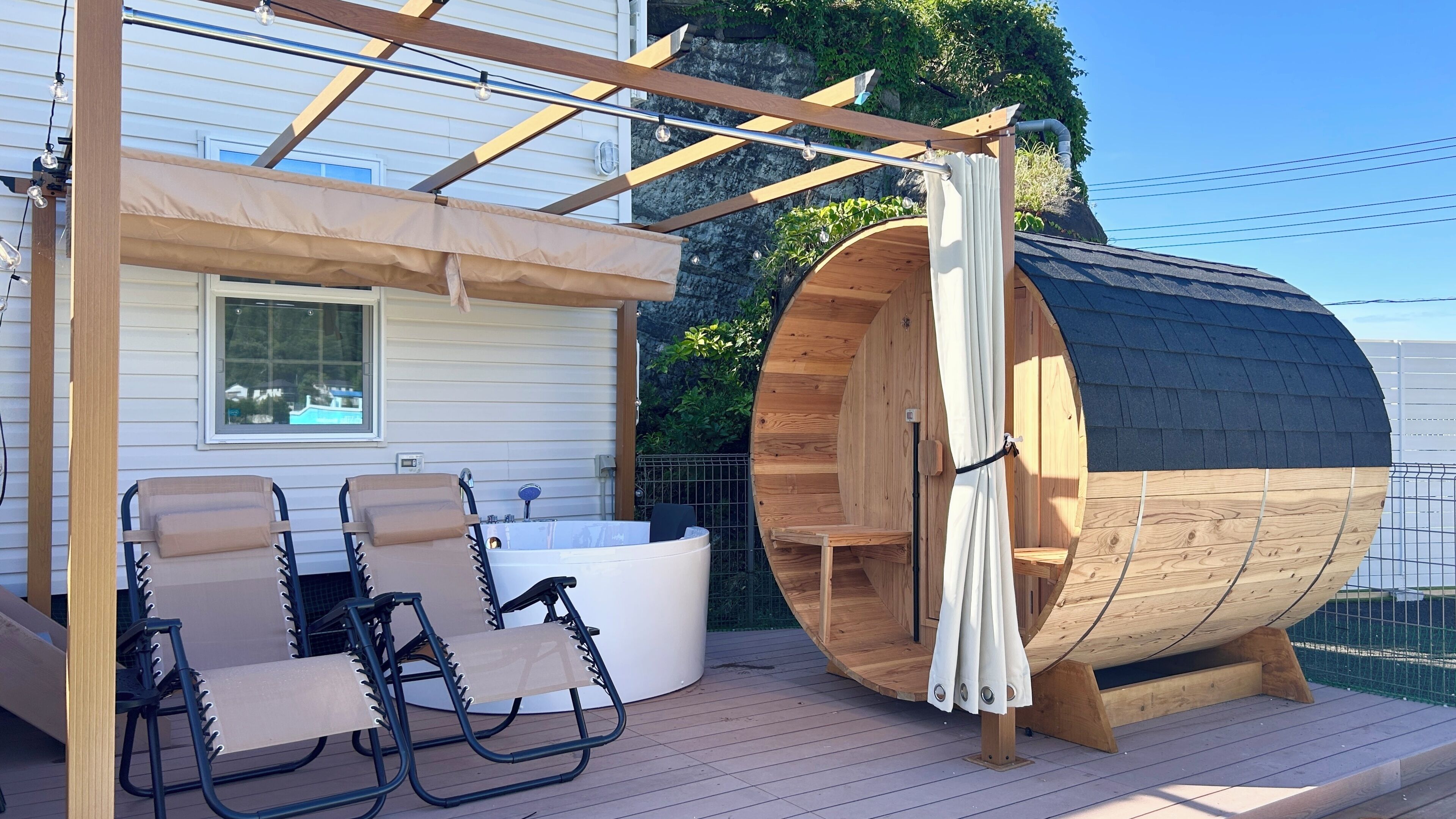 Una terraza de madera con un jacuzzi, dos sillones de descanso y una gran estructura de barril de madera.