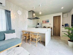 A modern kitchen with a central island, a dining area with a table and chairs, a sofa, and a potted plant. - Solana Beach Villa Minamiboso (Minamiboso)